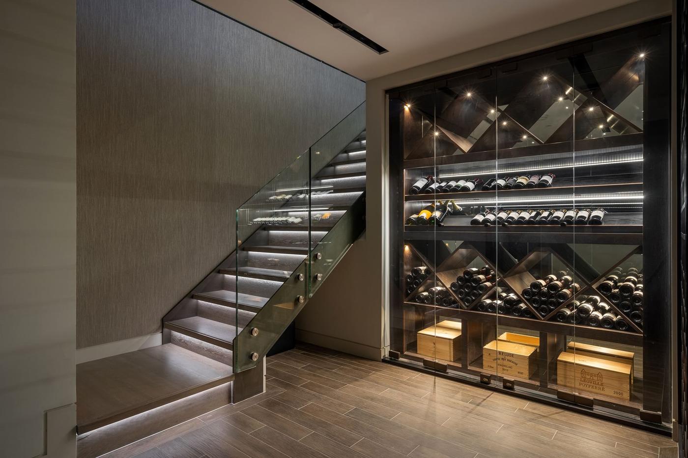 Wine cellar with shelves of wine bottles and wooden crates beside a staircase with glass railings