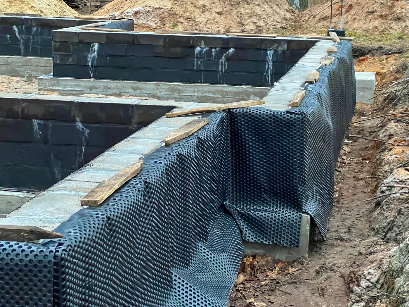 Foundation walls under construction with external waterproofing membrane and timber boards
