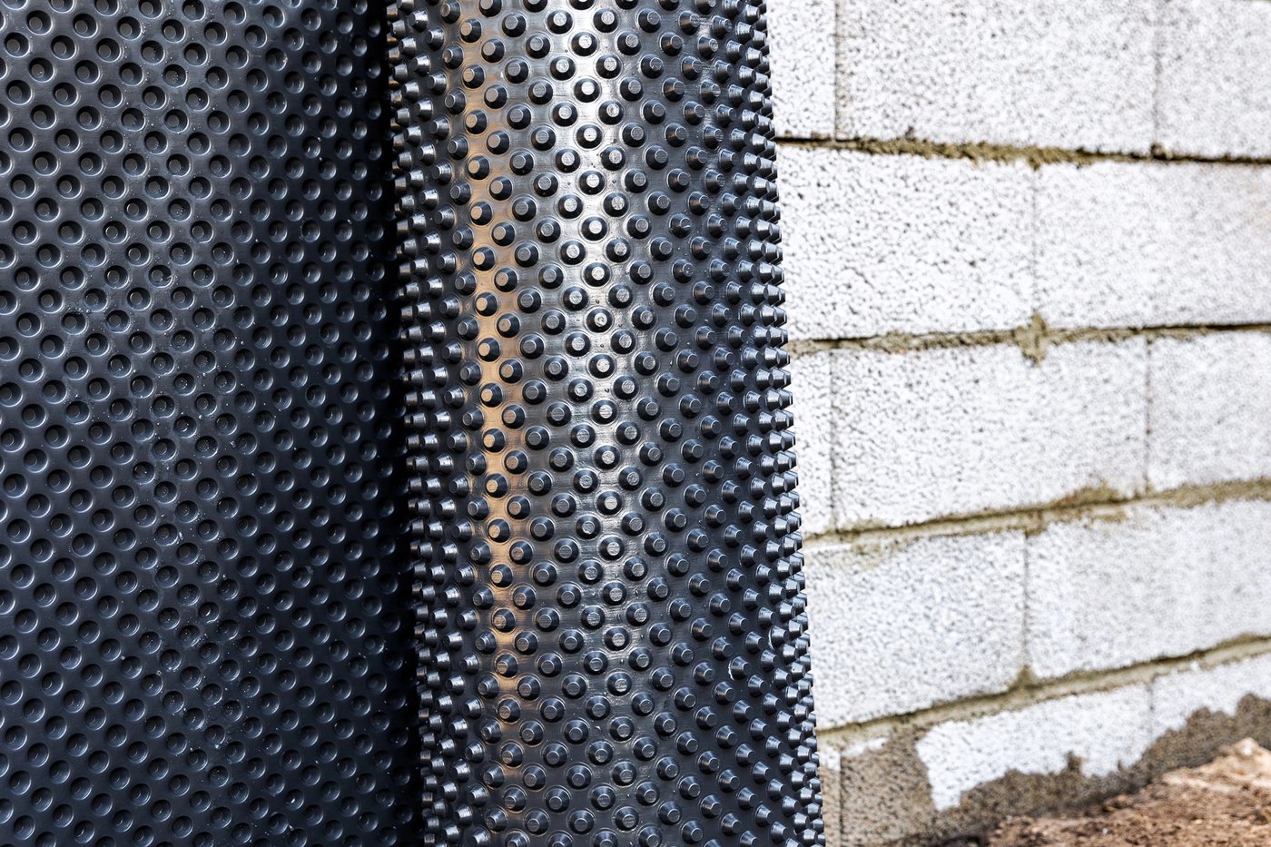 Close-up of a black dimpled waterproofing membrane fitted beside concrete foundation blocks