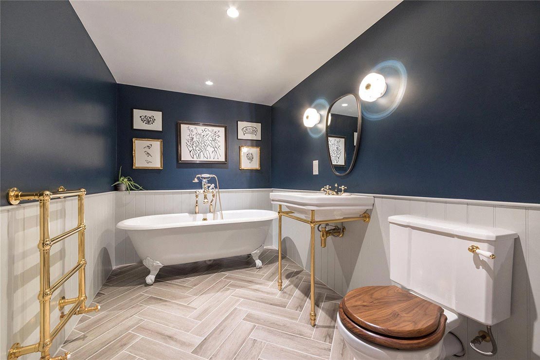 dark blue and white bathroom with wooden flooring, freestanding bath tub, toilet and sink with mirror