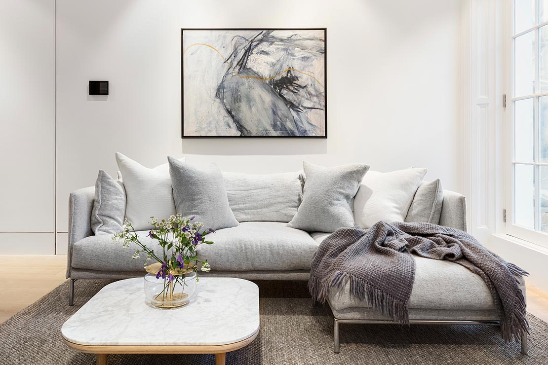 modern lounge with large grey couch, wooden floor with rug and white wall