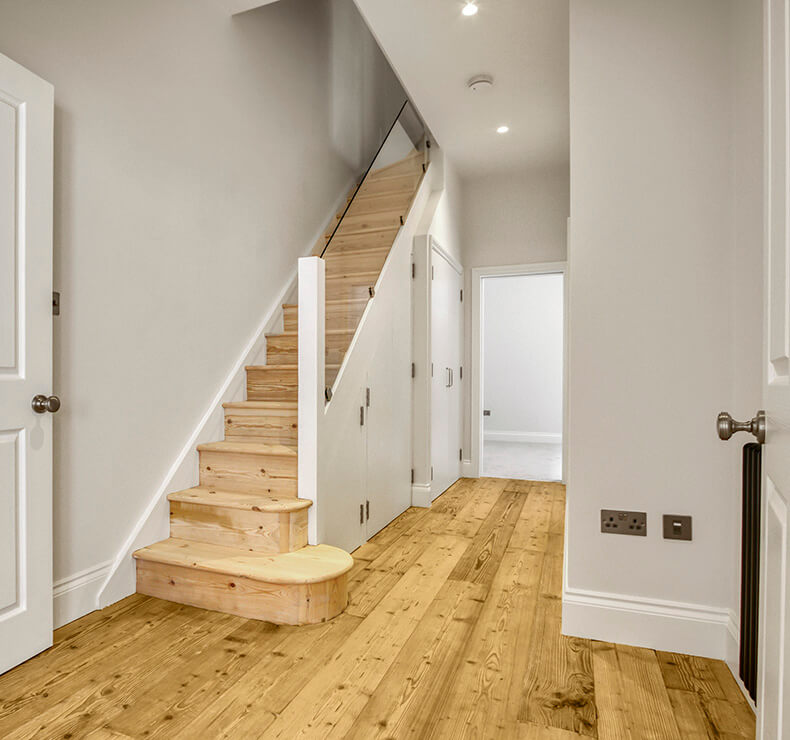 Light tan walls and brown modern wood flooring in a hallway room with stairs.
