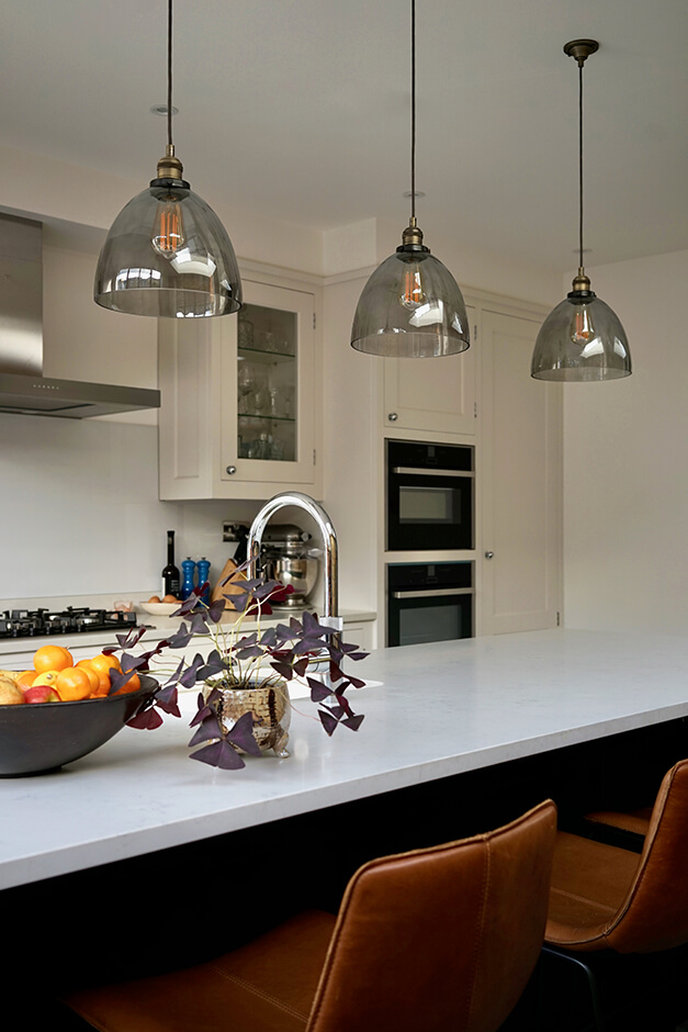 white kitchen island with modern tan brown bar stools and hanging lights