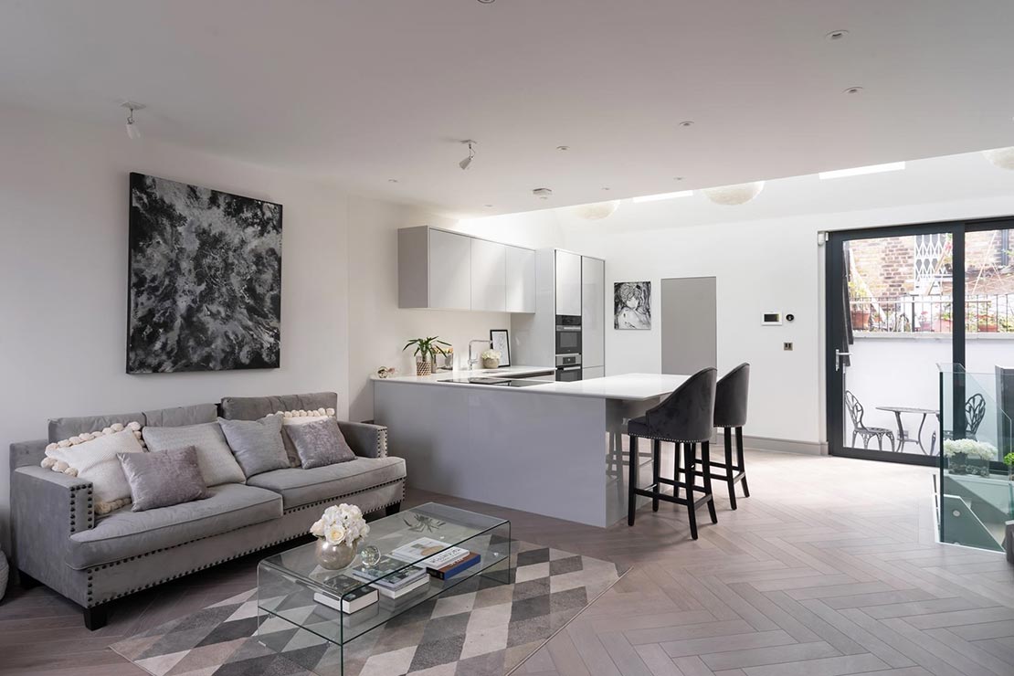 open plan grey and white kitchen and lounge area with wooden flooring, island with dining area