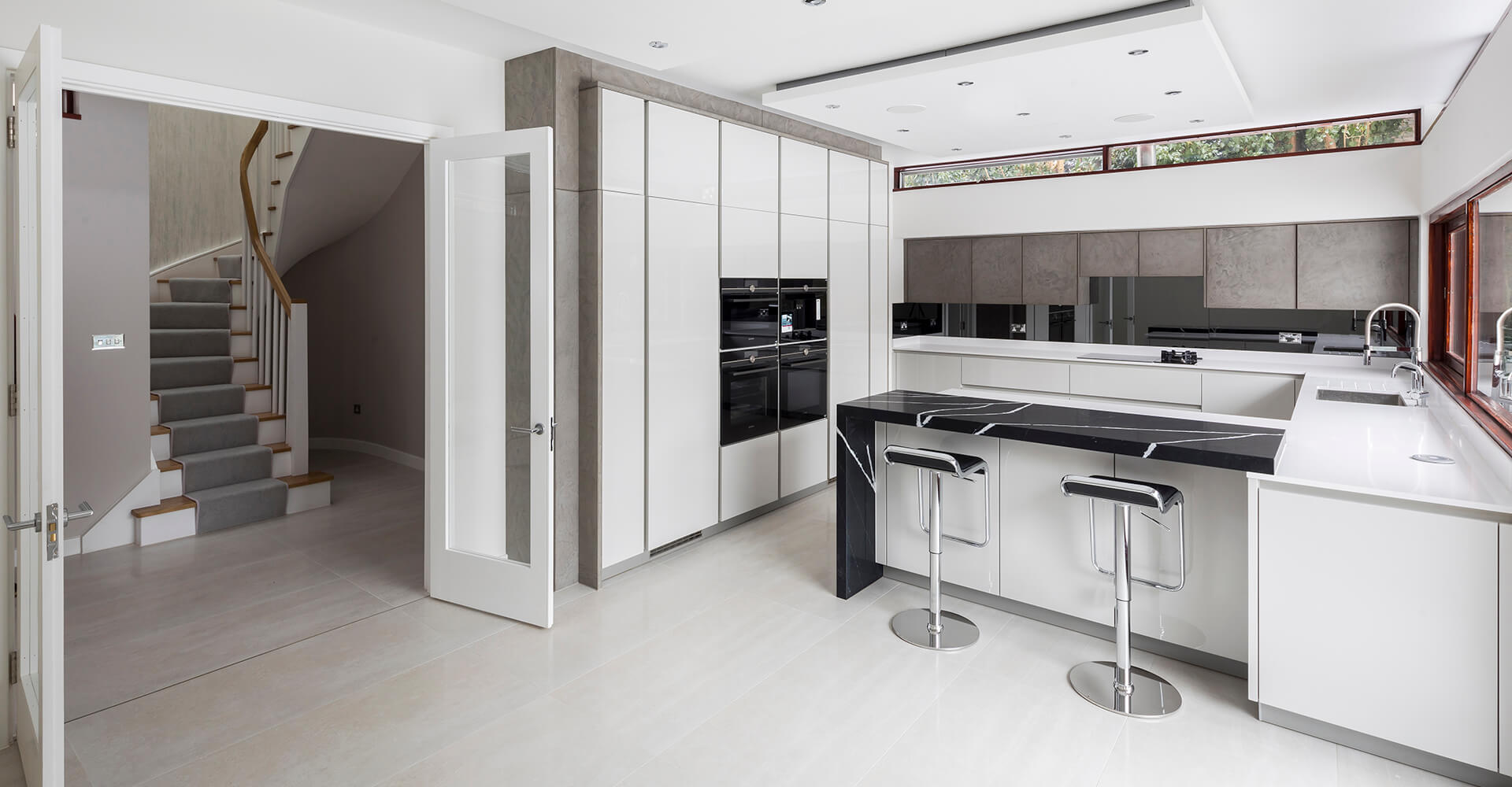 modern white and grey kitchen with black marble island, wall ovens and built in cabinets