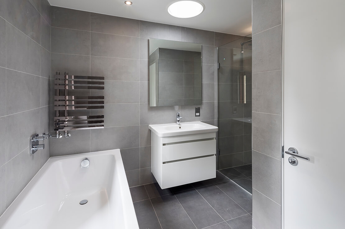 modern grey bathroom with white bathrub and sink with cabinet and mirror