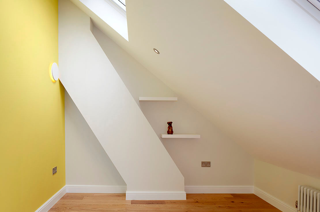 white and yellow walled space beneath staircase with suspended shelves, socket and wooden flooring 