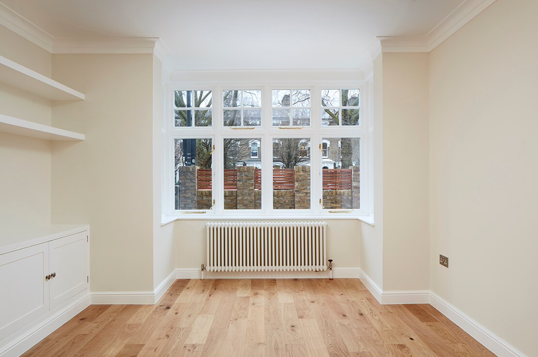 cream white room with woodern flooring, alcove with outer view and radiator