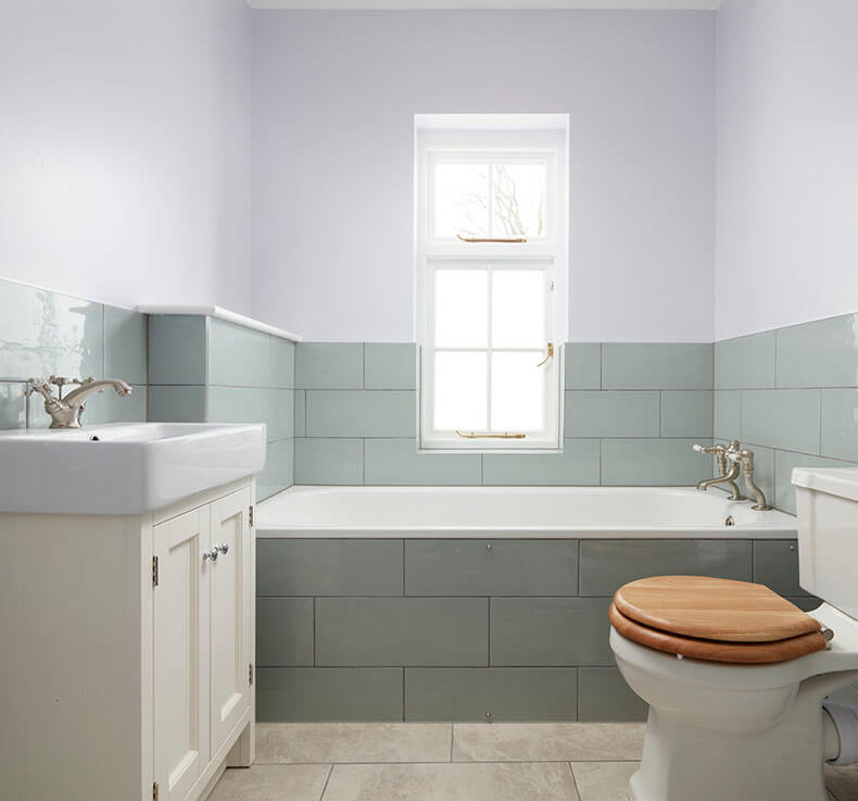 grey tiled bathroom with bath tub, sink with cabinet and toilet