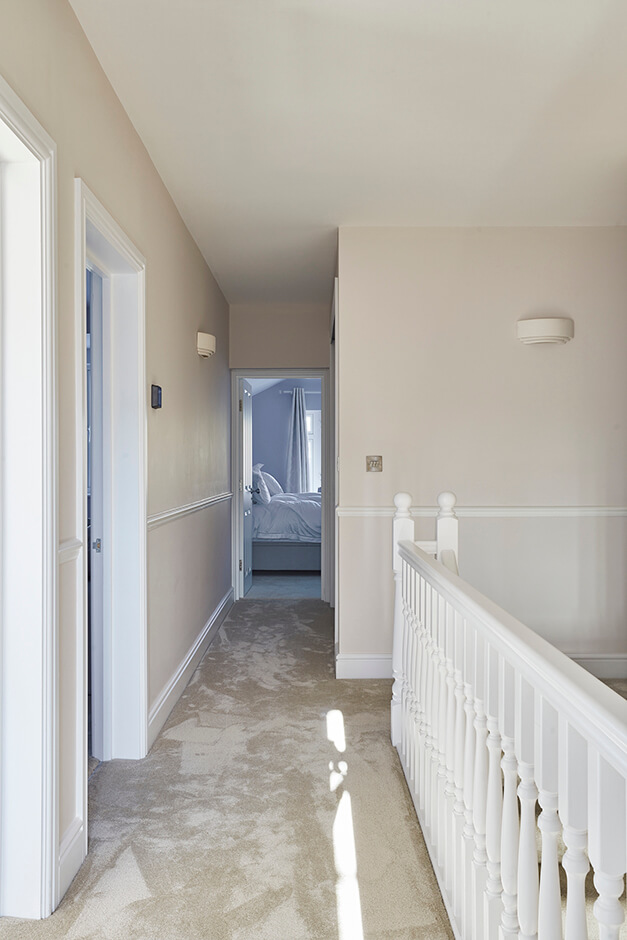 carpeted hallway with cream white walls and white railing