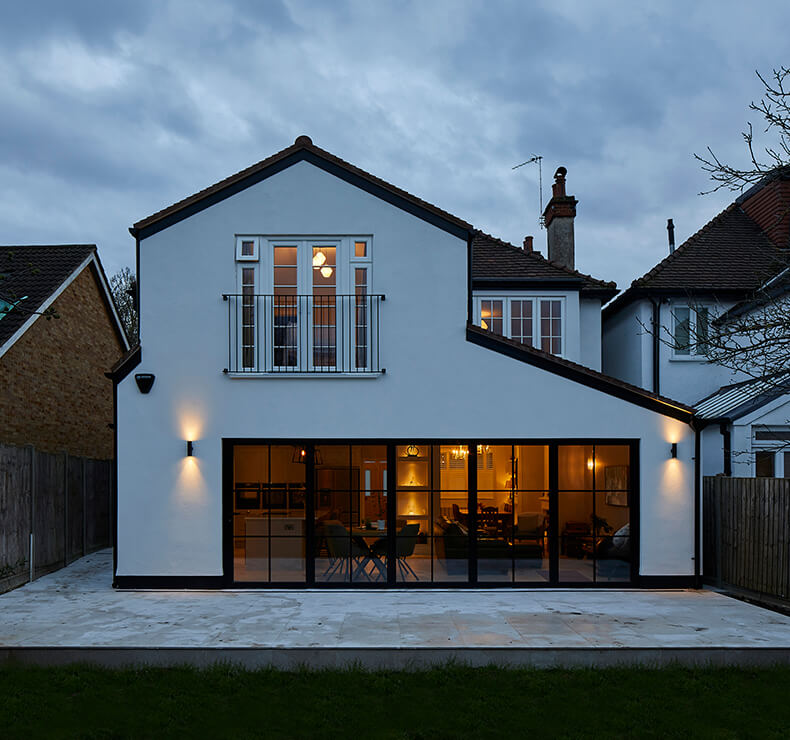 white house exterior rear view at nightwith black paned glass doors, patio and garden