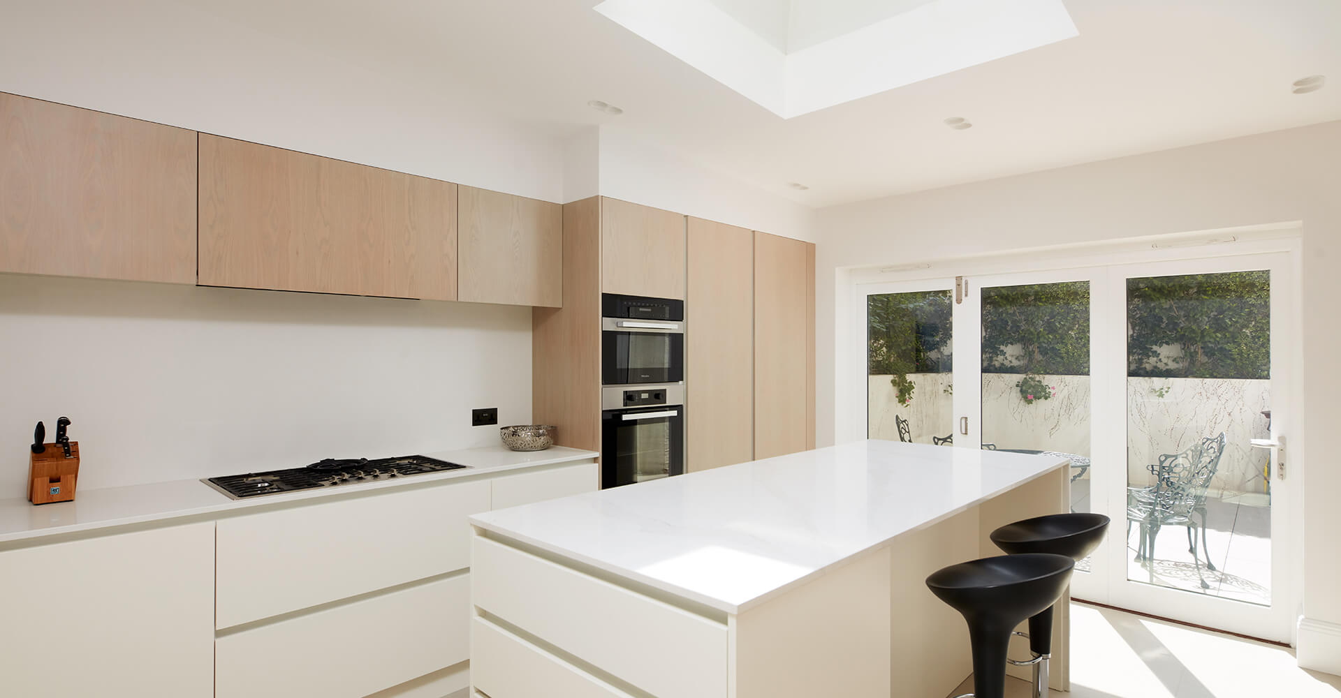 white modern kitchen with minimalist island, wall ovens and wooden built-in cabinets