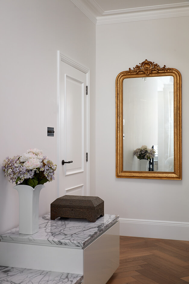 white bedroom entrance with wooden florring, large mirror and marble-top storage