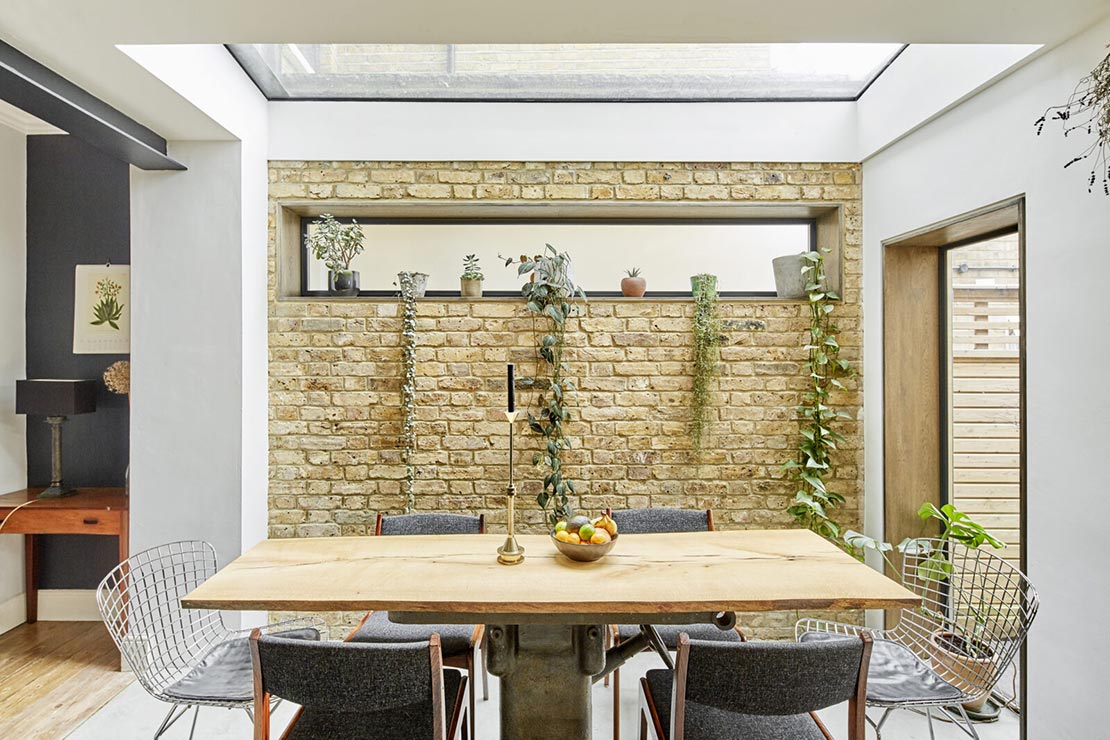 dining area with wooden dining table, skylight, and exposed brick interior wall