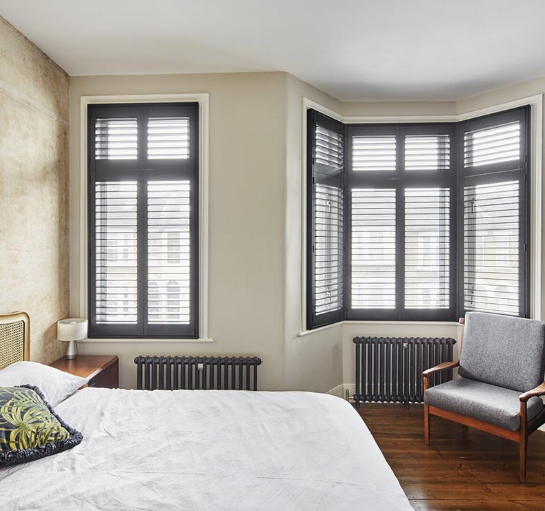 bedroom with black louvre windows, wooden flooring, and radiators
