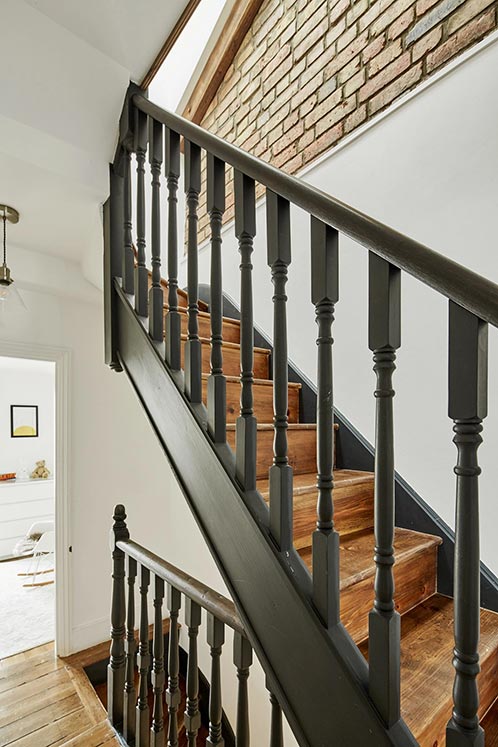 wooden staircase with black railing and exposed brick interior wall