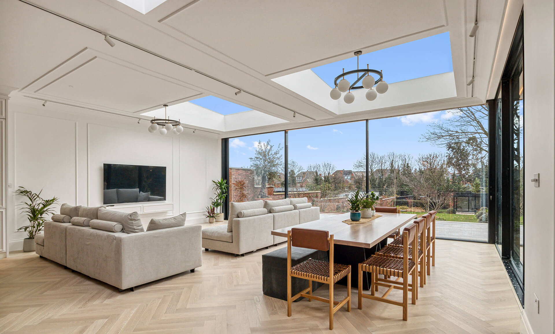 Modern rear houme extension with light taupe, dark charcoal, and dark rust wood flooring and table design.