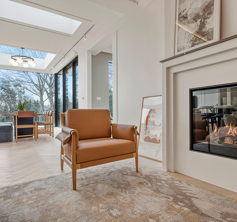Armchair in a modern domestic room with light beige and dark rust brown flooring, in the backround vissible bifold doors and table with chairs.