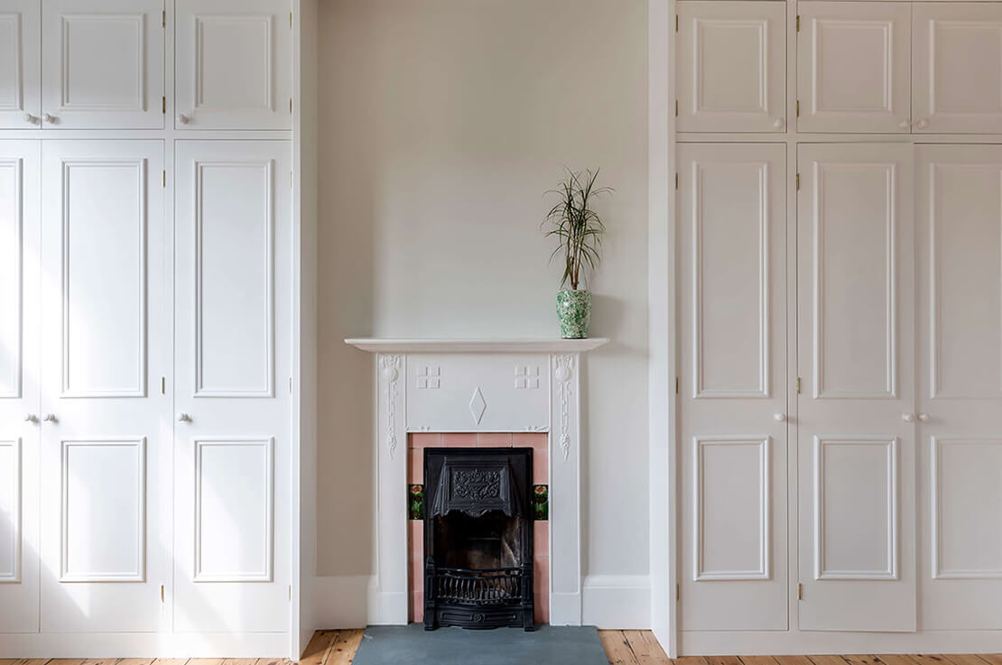 room with small fire place, white walls, white wardrobes and wooden floors